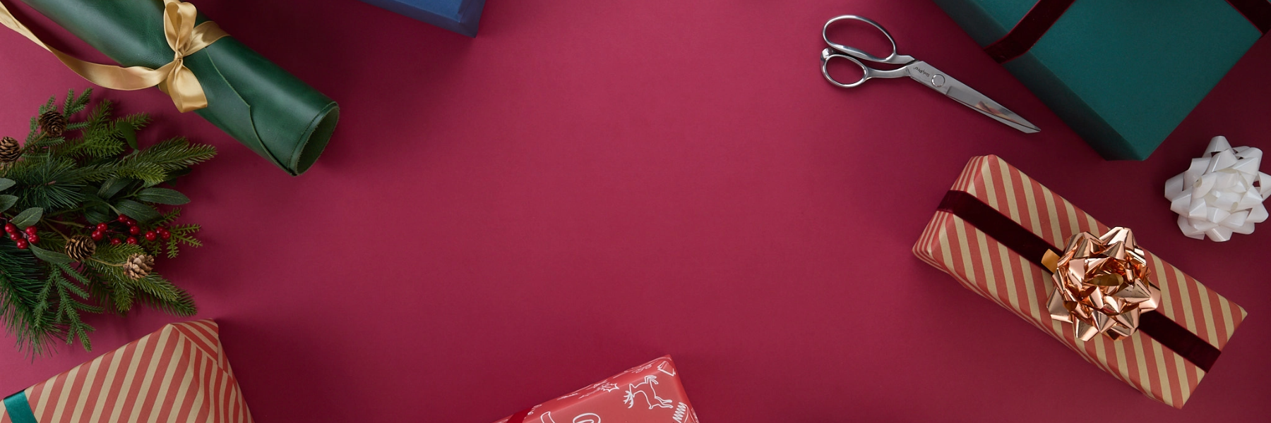 Rolled leather, greenery, wrapped gift boxes and wrapping supplies surround a red backdrop