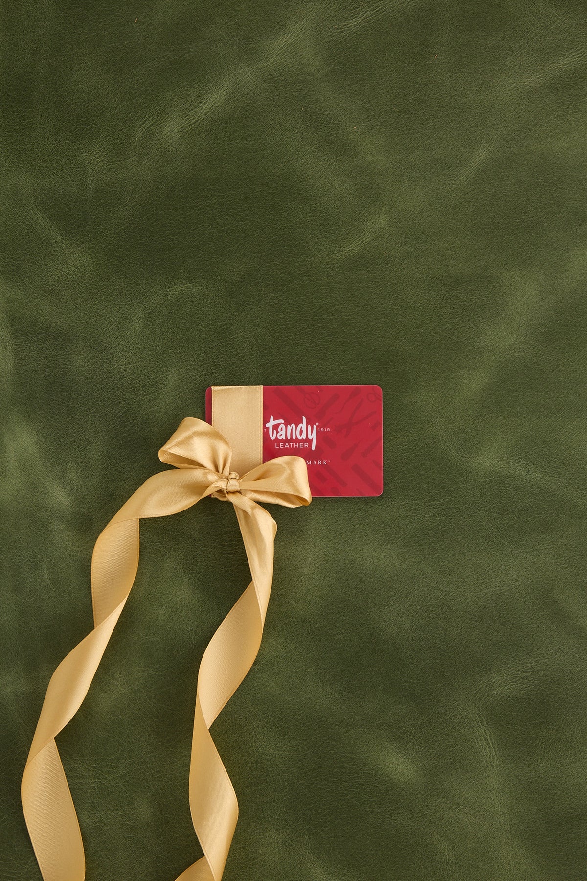 Tandy Leather Gift Card wrapped in ribbon on top of green pull-up leather