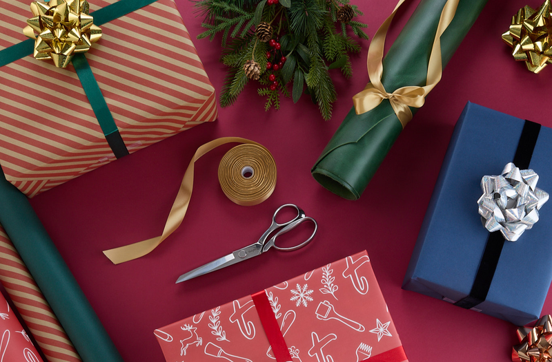 Rolled leather, greenery, wrapped gift boxes and wrapping supplies surround a red backdrop